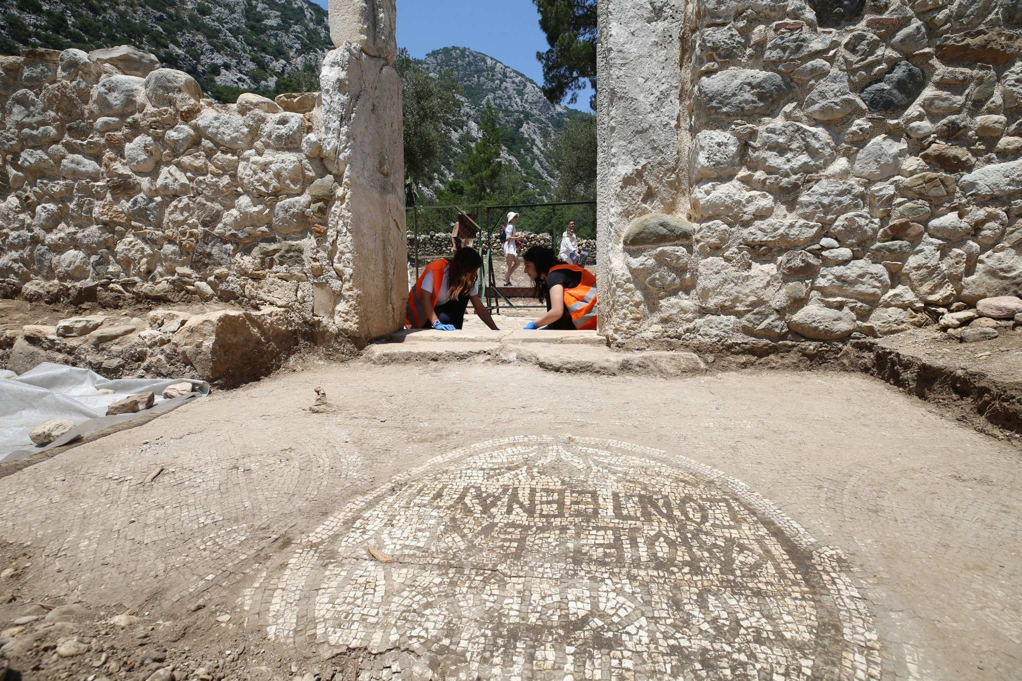 Two archaeologists examine a Byzantine mosaic inscription at the entrance of a stone church in Olympos Ancient City, Türkiye